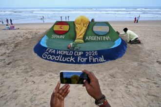 مشجعون يتفاعلون مع مجسم لكأس العالم في استاد كرة قدم.