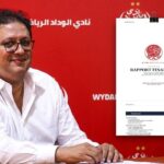 رجل أمام لوحة حمراء تحمل شعار نادي الوداد.
