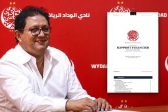 رجل أمام لوحة حمراء تحمل شعار نادي الوداد.