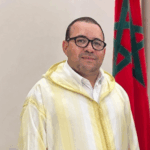 يوسف أمنزو يتحدث وراء منصة، علم المغرب خلفه