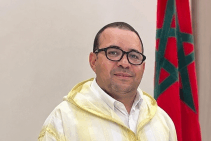 يوسف أمنزو يتحدث وراء منصة، علم المغرب خلفه