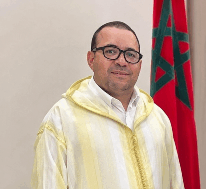 يوسف أمنزو يتحدث وراء منصة، علم المغرب خلفه