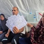 أحمد السيقلي جالسًا مع عائلته في ملجأ مؤقت بغزة.