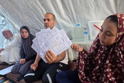 أحمد السيقلي جالسًا مع عائلته في ملجأ مؤقت بغزة.