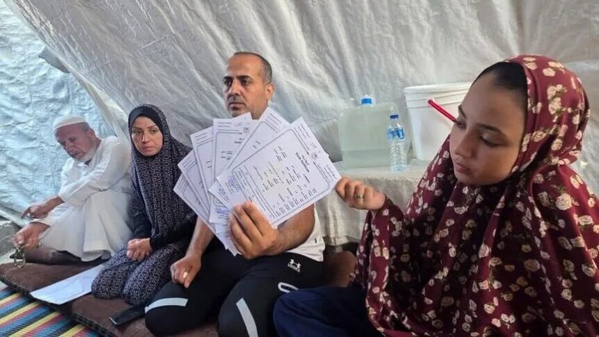 أحمد السيقلي جالسًا مع عائلته في ملجأ مؤقت بغزة.