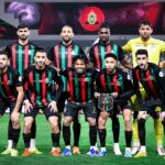 لاعبو الجيش الملكي بقمصان مخططة حمراء وسوداء على أرضية الملعب.