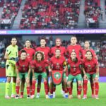 منتخب المغرب النسوي لكرة القدم يرتدي زياً رياضياً ويقف في الملعب.