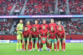 منتخب المغرب النسوي لكرة القدم يرتدي زياً رياضياً ويقف في الملعب.