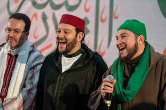 ثلاثة رجال يرتدون ملابس تقليدية يبتسمون للكاميرا.