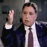 رجل أعمال يرتدي بدلة ويتحدث أمام الكاميرا.