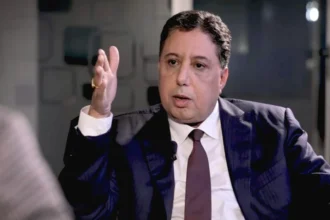 رجل أعمال يرتدي بدلة ويتحدث أمام الكاميرا.