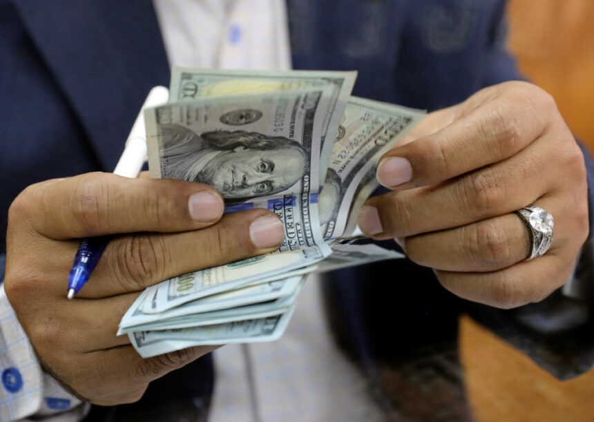 رجل يحمل قلماً ومجموعة أوراق نقدية من فئة المئة دولار