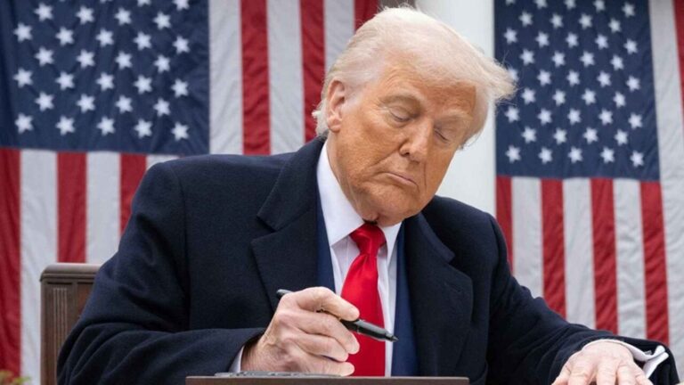 دونالد ترامب يوقع وثائق رسمية أمام العلم الأمريكي.