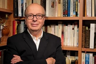 رجل يرتدي بدلة سوداء وقميص أبيض في غرفة بها كتب.