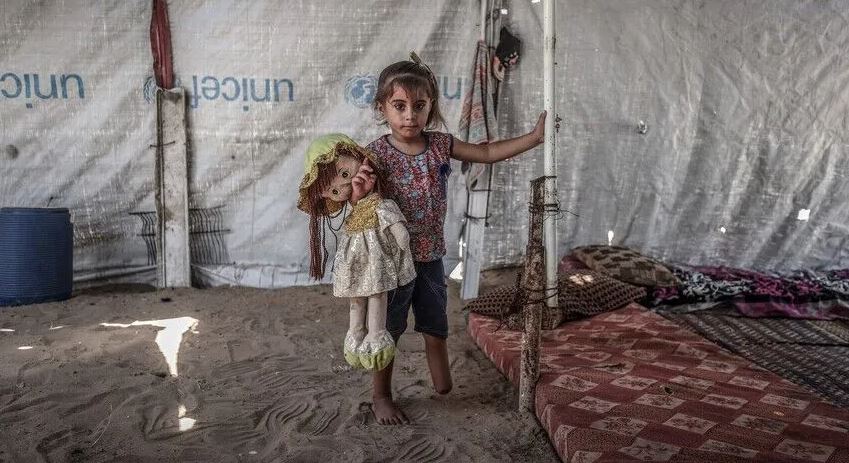 طفلة فلسطينية تحمل دمية داخل خيمة نزوح في غزة.