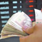 يد تحمل ورقة نقدية بجانب آلة حاسبة