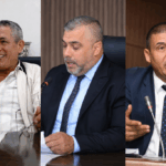 ثلاثة رجال أعمال يتحدثون إلى الميكروفونات ويحملون وثائق