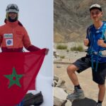 شابان يقفان على قمة جبل، أحدهما يرفع علم المغرب.