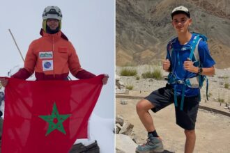شابان يقفان على قمة جبل، أحدهما يرفع علم المغرب.