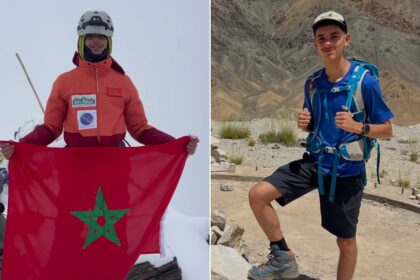 شابان يقفان على قمة جبل، أحدهما يرفع علم المغرب.