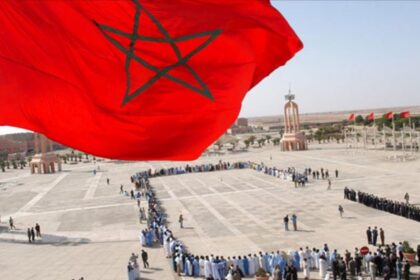 أشخاص يقفون بانتظام أمام مسجد في الصحراء.