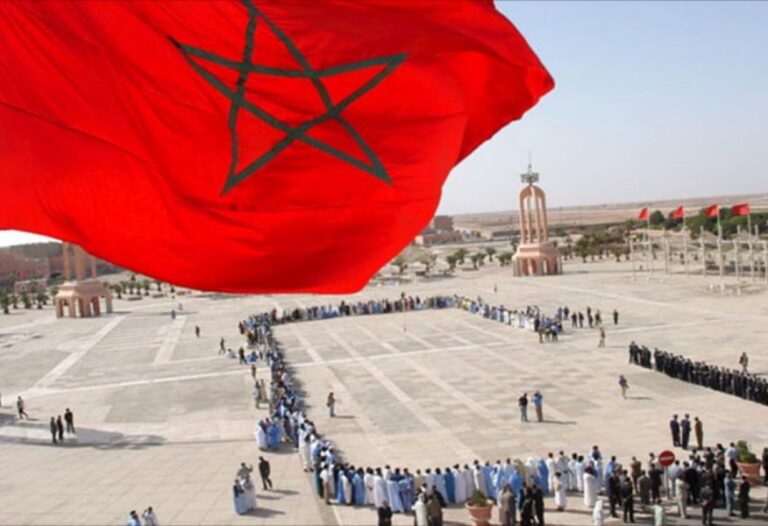 أشخاص يقفون بانتظام أمام مسجد في الصحراء.