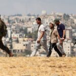 فلسطينيون وإسرائيليون يسيرون في حقل مفتوح قرب قاعدة عسكرية.