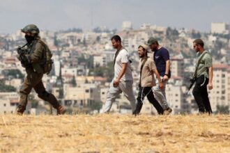 فلسطينيون وإسرائيليون يسيرون في حقل مفتوح قرب قاعدة عسكرية.