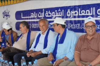 أشخاص يجلسون أمام لافتة زرقاء عليها كتابات