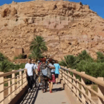 أشخاص يعبرون جسراً أمام جبل أحمر كبير.