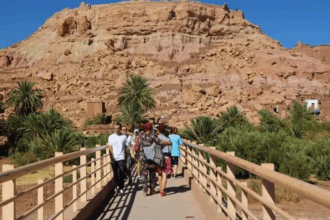 أشخاص يعبرون جسراً أمام جبل أحمر كبير.