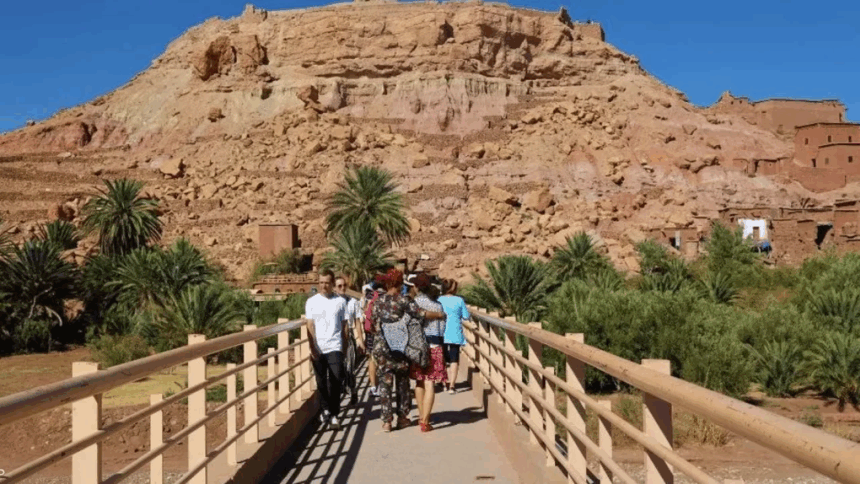 أشخاص يعبرون جسراً أمام جبل أحمر كبير.