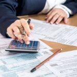 شخص يحسب باستخدام آلة حاسبة وقلم بجانبه.