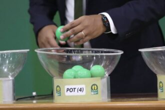 لاعب يسحب قرعة من وعاء زجاجي شفاف.