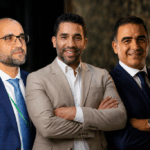 ثلاثة رجال يرتدون قمصاناً بيضاء، يتحدثون في مكان مغلق.