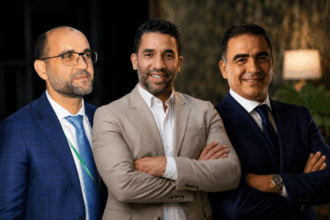 ثلاثة رجال يرتدون قمصاناً بيضاء، يتحدثون في مكان مغلق.
