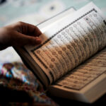 شخص يحمل مصحفاً مفتوحاً ويشير بيده إلى آياته