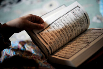 شخص يحمل مصحفاً مفتوحاً ويشير بيده إلى آياته