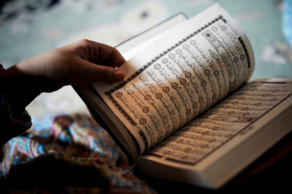 شخص يحمل مصحفاً مفتوحاً ويشير بيده إلى آياته