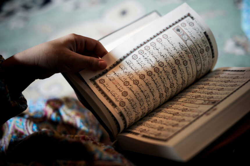 شخص يحمل مصحفاً مفتوحاً ويشير بيده إلى آياته