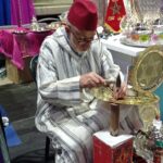 رجل بقبعة حمراء أمام طاولة عليها أكواب شاي وفخار