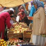 نساء يتفحصن صناديق فواكه وخضروات طازجة في سوق.