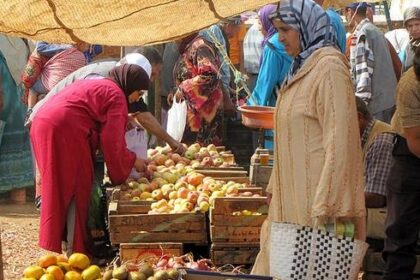 نساء يتفحصن صناديق فواكه وخضروات طازجة في سوق.