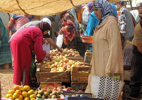 نساء يتفحصن صناديق فواكه وخضروات طازجة في سوق.