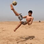 شاب مغربي يلعب كرة القدم على الشاطئ بمهارة.