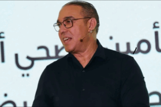 رجل يرتدي نظارة أمام الميكروفونات يتحدث