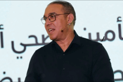 رجل يرتدي نظارة أمام الميكروفونات يتحدث