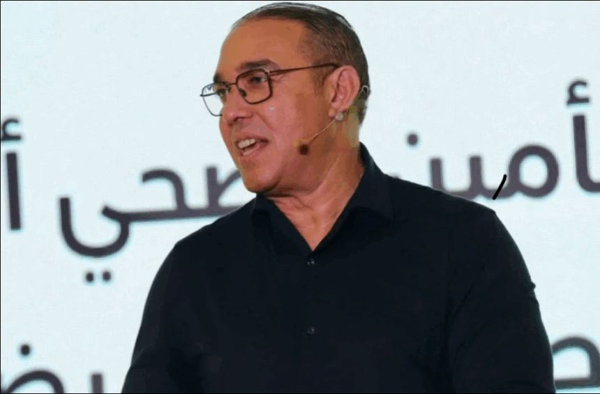 رجل يرتدي نظارة أمام الميكروفونات يتحدث