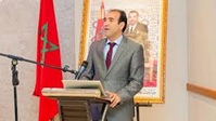 رجل يرتدي بدلة يلقي خطابًا بجوار علم المغرب