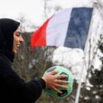امرأة مبتسمة تحمل كرة قدم خضراء.